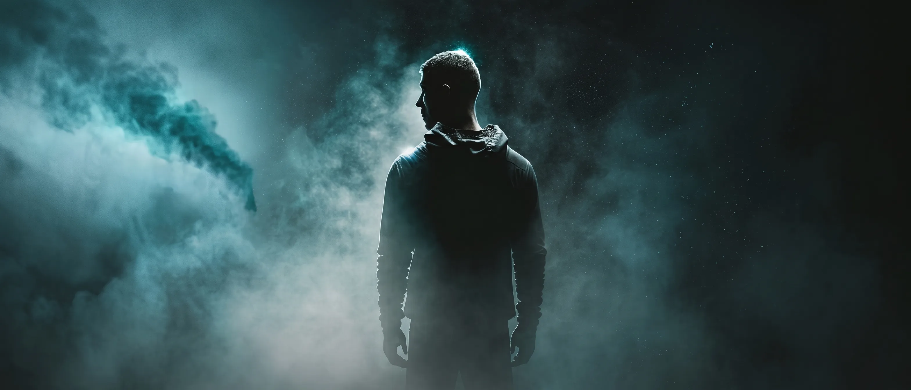 A silhouetted man in a hoodie stands facing away in a dark, drifting fog lit by cold teal light.